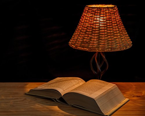 Person reading a physical book under a warm lamp at night